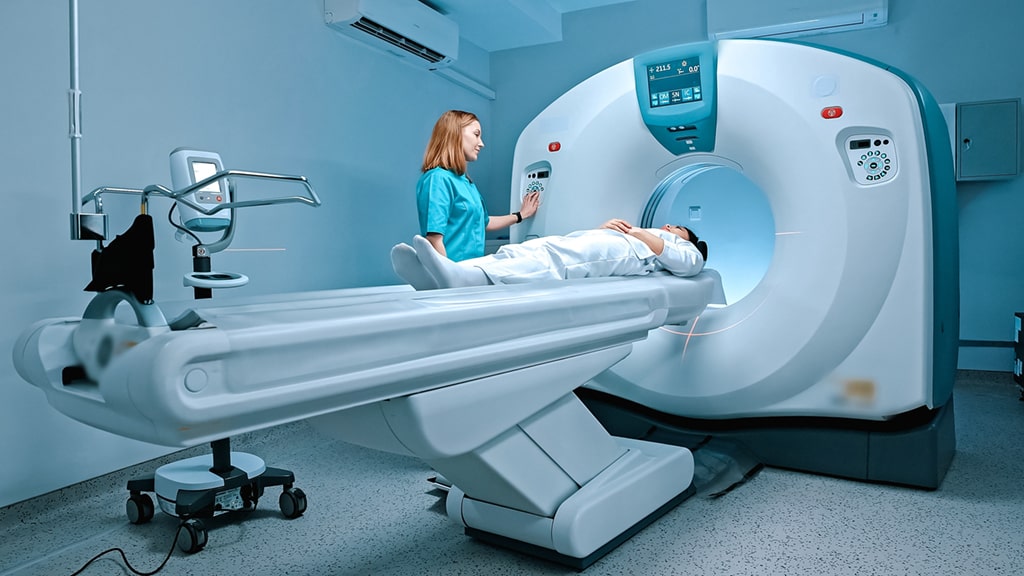 A medical professional operating a CT scan machine with a patient lying on the examination table.